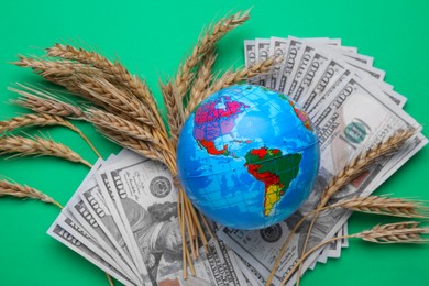 Photo of Import and export concept. Globe, ears of wheat and money on green background, flat lay