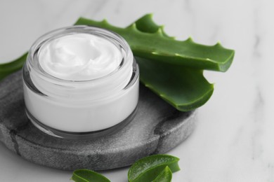 Jar with cream and cut aloe leaves on white marble table, closeup