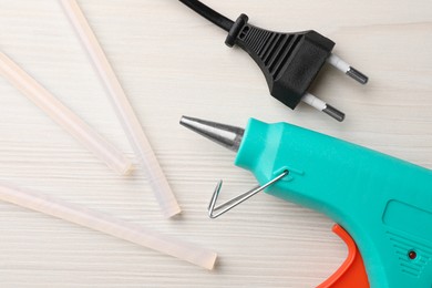 Photo of Turquoise glue gun and sticks on white wooden table, flat lay