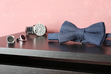 Photo of Stylish blue bow tie, cufflinks and wristwatch on wooden table