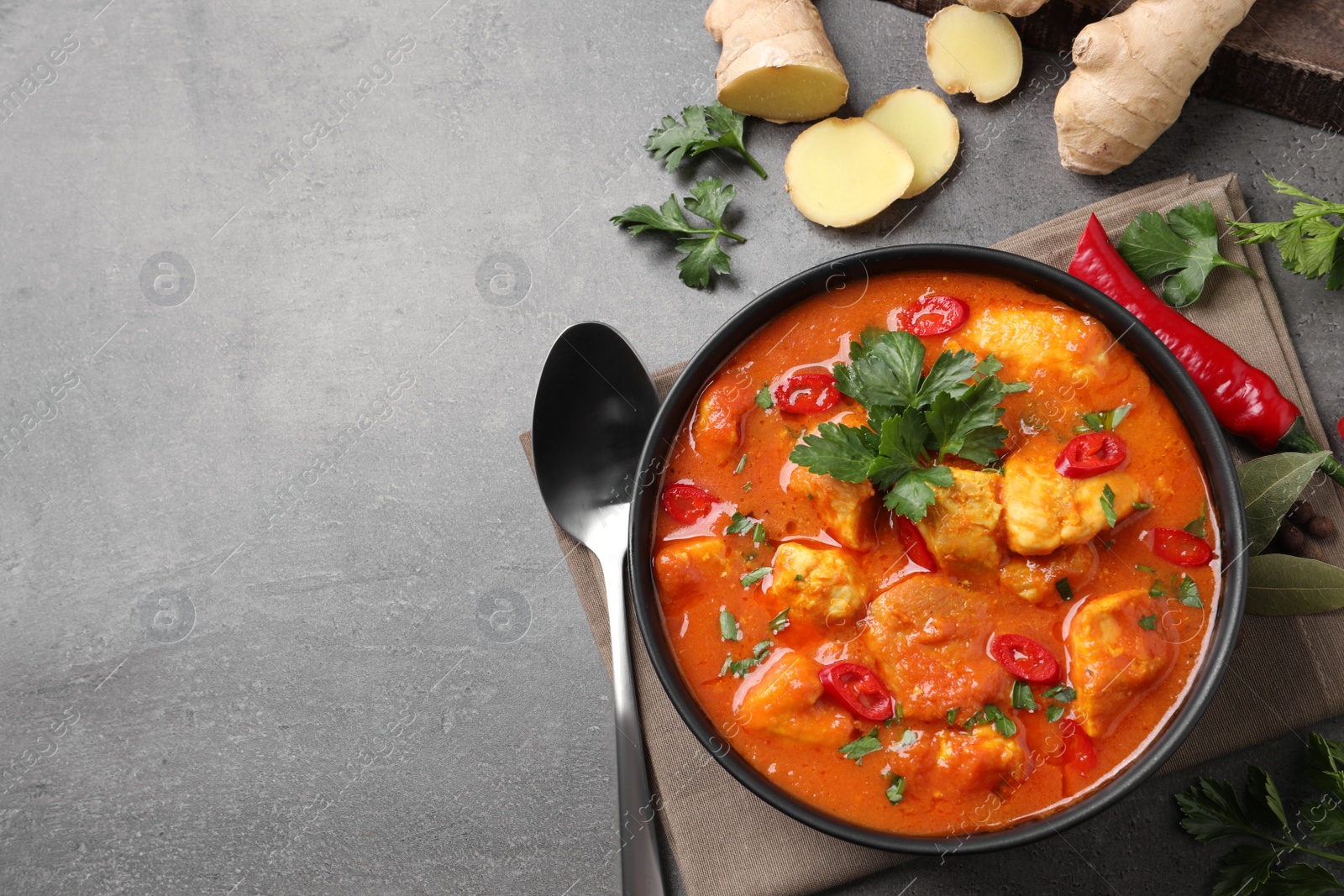 Photo of Bowl of delicious chicken curry on grey table, flat lay. Space for text