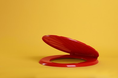 New red plastic toilet seat on yellow background
