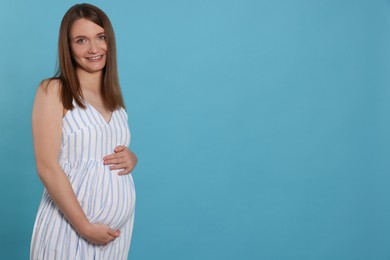 Photo of Happy young pregnant woman on light blue background. Space for text