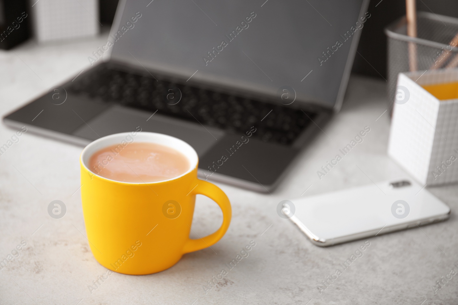 Photo of Yellow cup with coffee and phone near laptop on office table. Break time