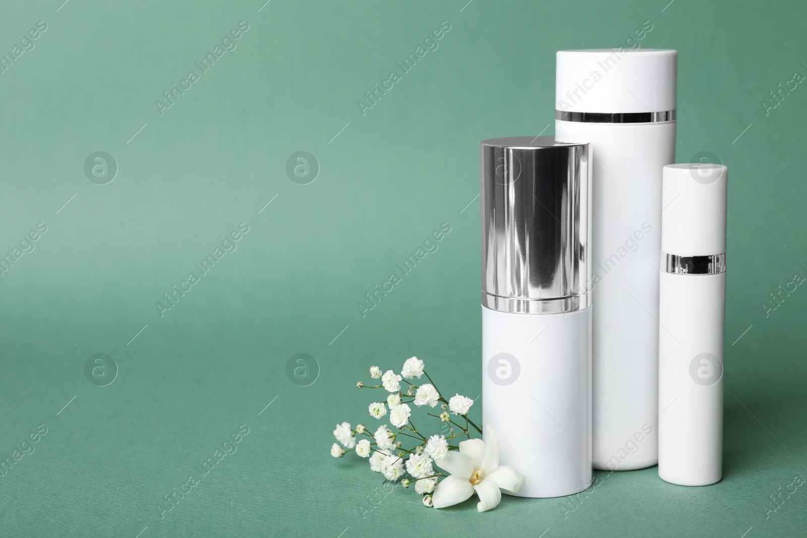 Photo of Set of luxury cosmetic products and flowers on blue-green background. Space for text