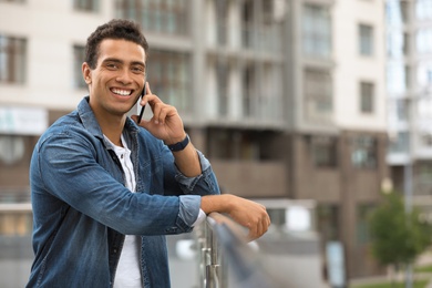 Portrait of handsome young African-American man talking on mobile phone outdoors. Space for text