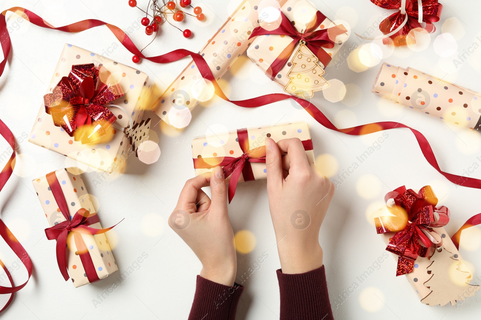 Photo of Woman holding Christmas gift box with red bow at white table, top view