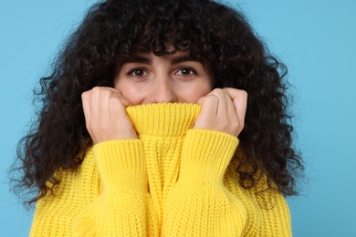 Young woman in stylish yellow sweater on light blue background