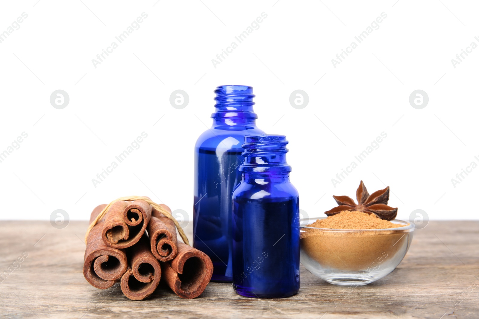 Photo of Bottles of essential oils, cinnamon sticks and powder on wooden table against white background