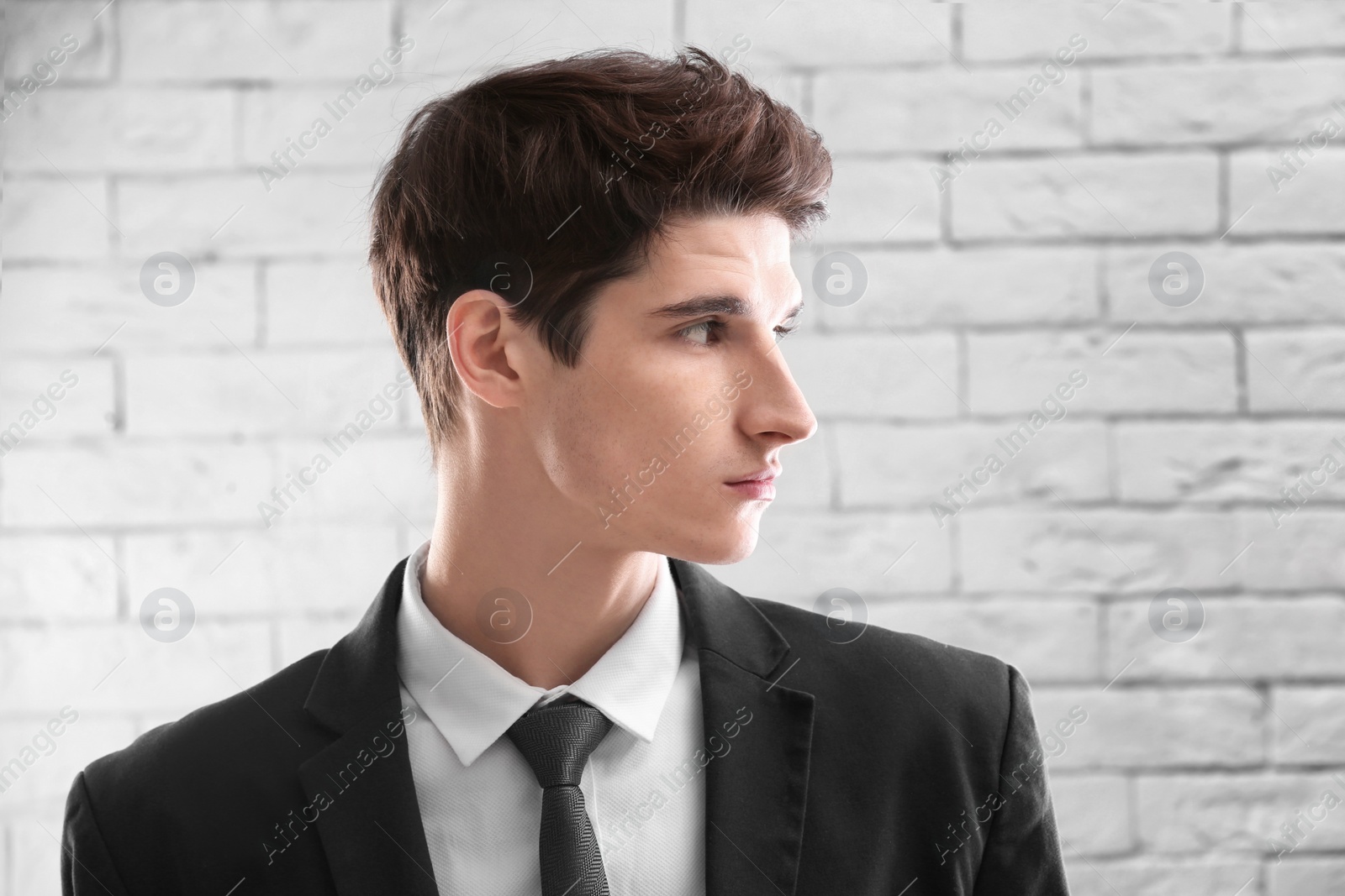 Photo of Portrait of young businessman with beautiful hair on brick wall background