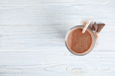 Glass of tasty chocolate milk on wooden background, top view with space for text. Dairy drink