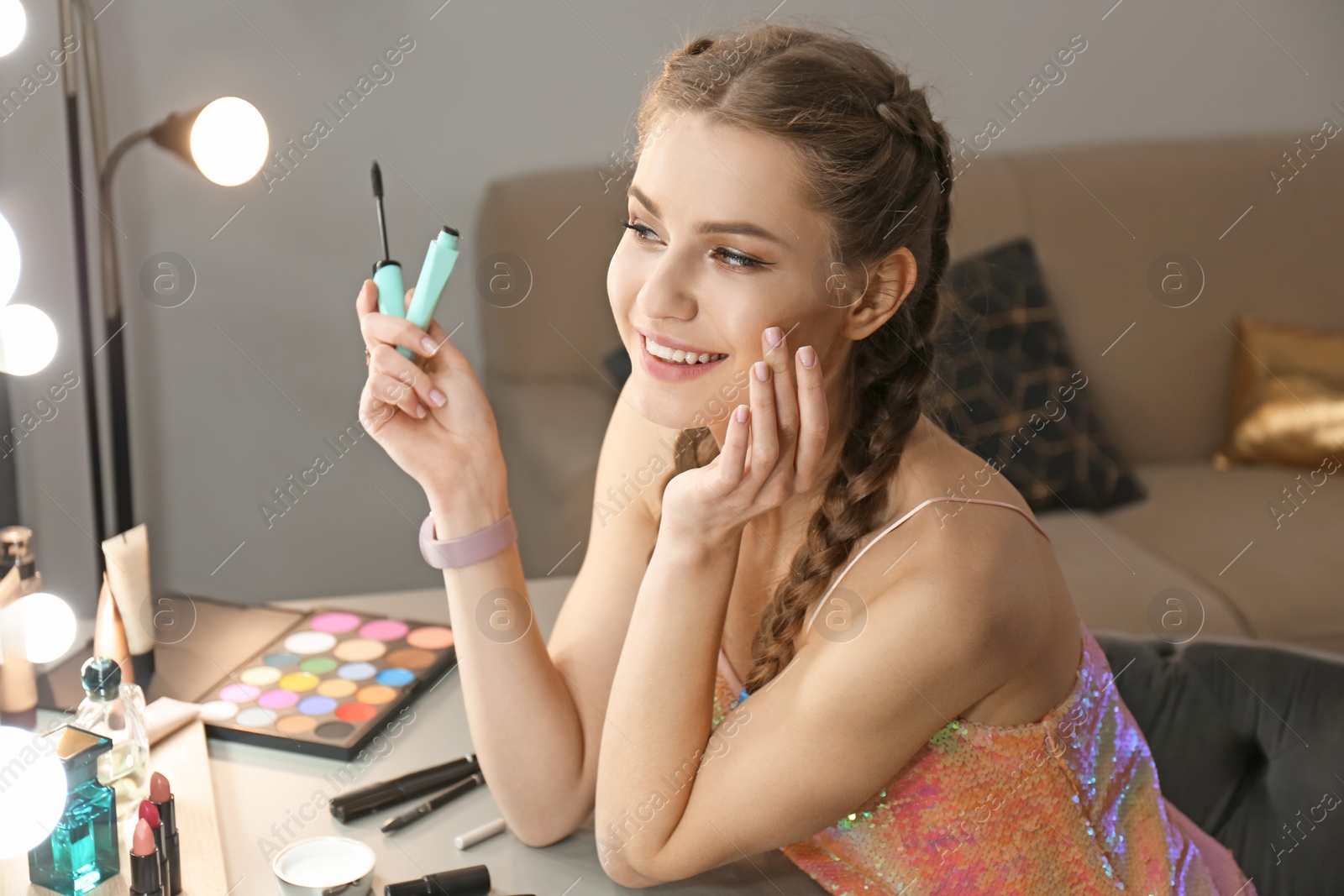 Photo of Portrait of beautiful woman applying makeup near mirror indoors