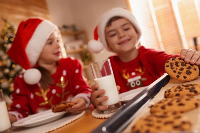 Photo of Cute little children with delicious Christmas cookies and milk at home, focus on pastry