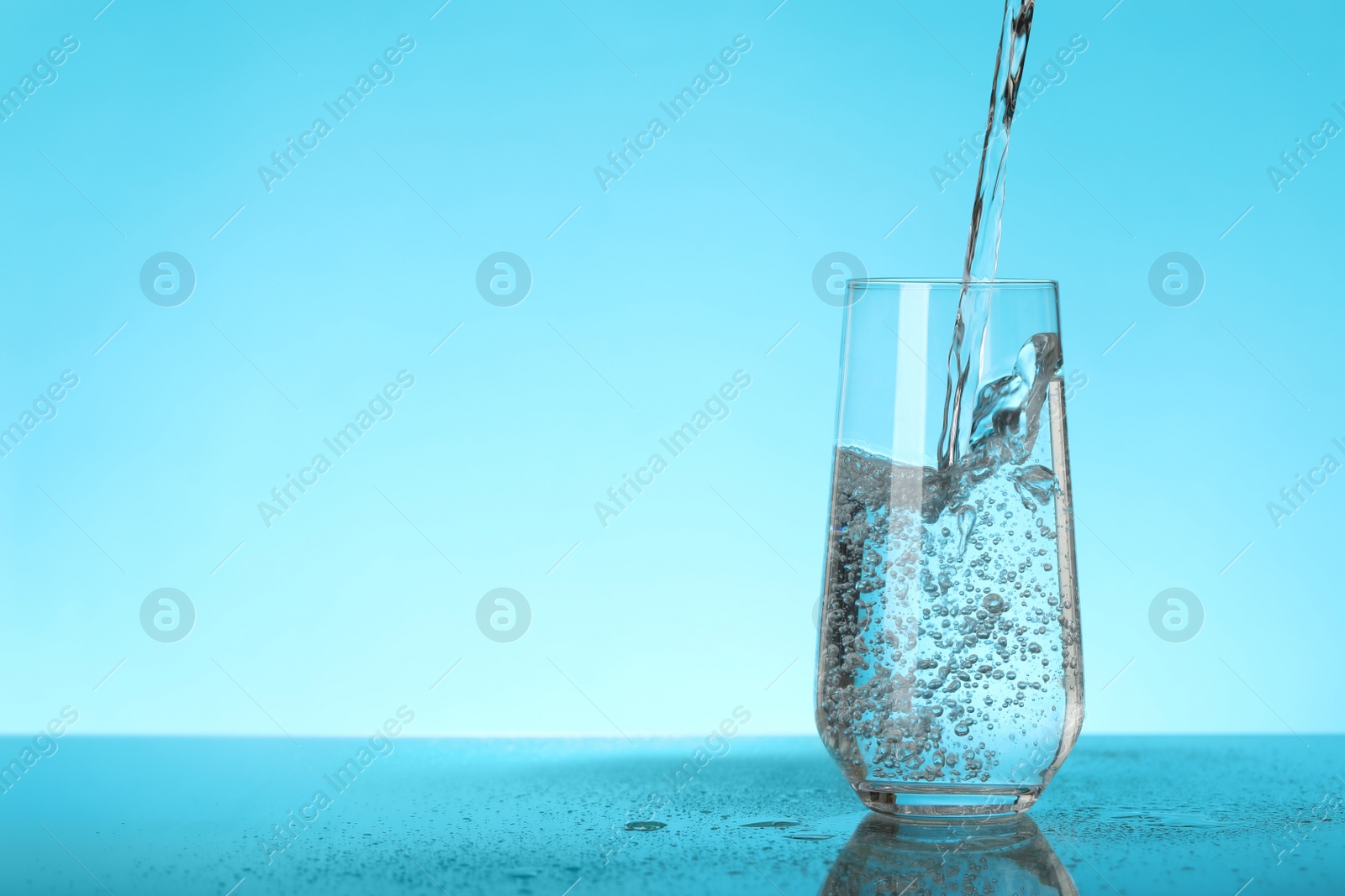 Photo of Pouring water into glass on blue background, space for text. Refreshing drink