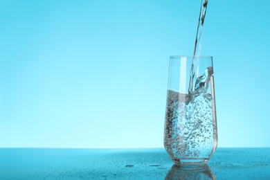 Photo of Pouring water into glass on blue background, space for text. Refreshing drink