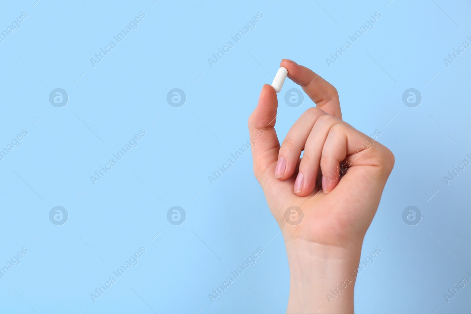 Photo of Woman holding vitamin capsule on light blue background, closeup. Space for text