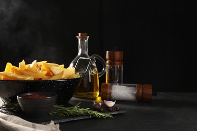 Composition with bowl of steaming baked potatoes, sauce and spices on black table