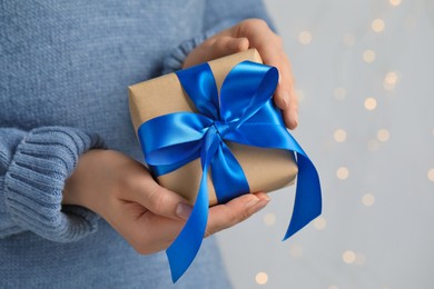 Photo of Woman holding gift box with blue bow against blurred festive lights, closeup and space for text. Bokeh effect