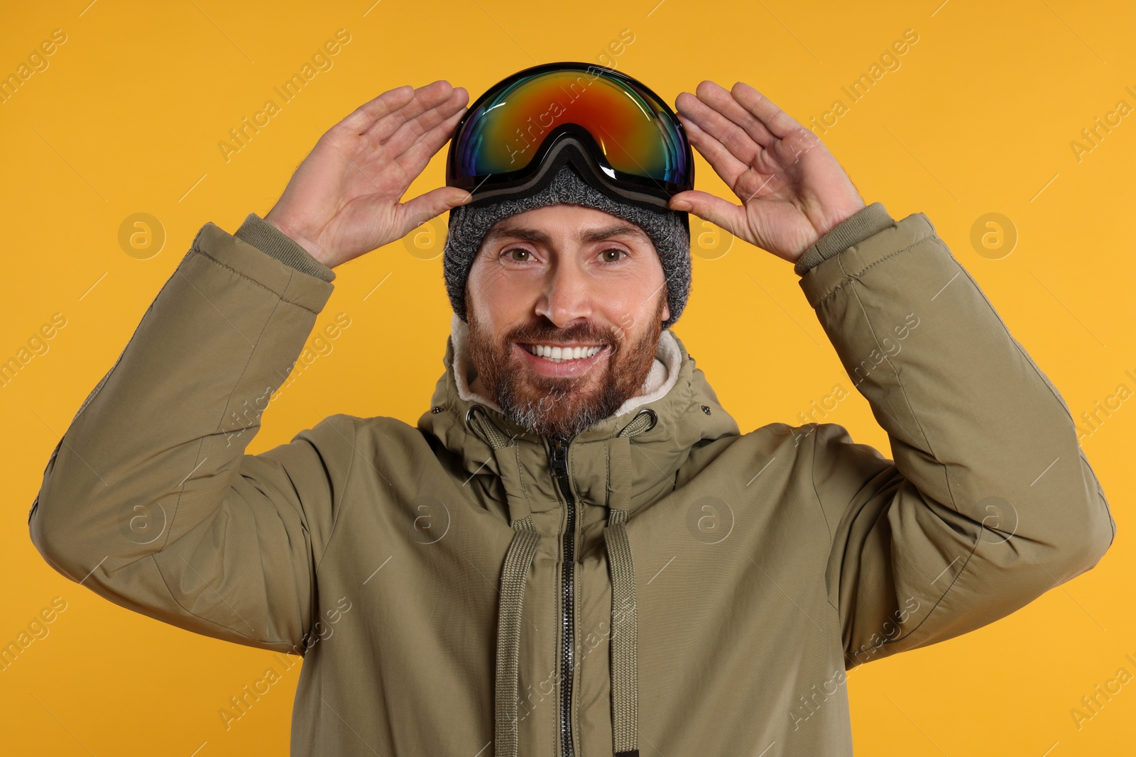 Photo of Winter sports. Happy man in ski suit and goggles on orange background