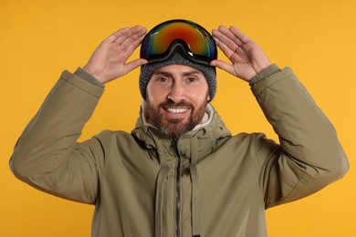 Photo of Winter sports. Happy man in ski suit and goggles on orange background