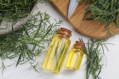 Photo of Bottles of essential oil and fresh tarragon sprigs on white wooden table, flat lay