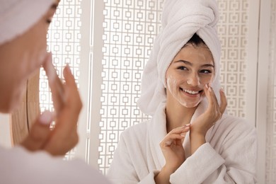 Beautiful teenage girl applying cleansing foam onto face near mirror at home. Skin care cosmetic