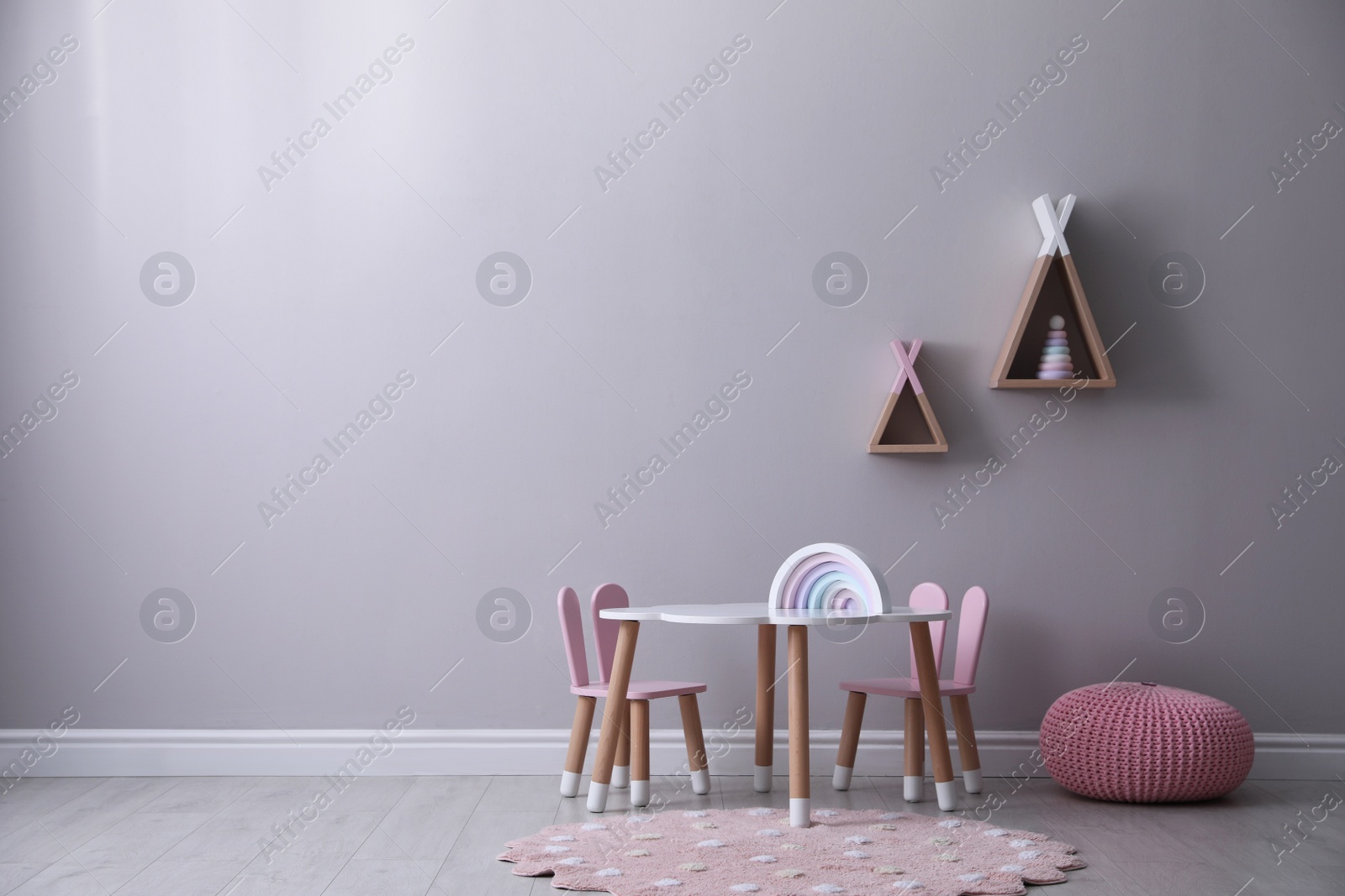 Photo of Cute child room interior with furniture, toys and wigwam shaped shelves on grey wall. Space for text