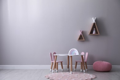 Cute child room interior with furniture, toys and wigwam shaped shelves on grey wall. Space for text