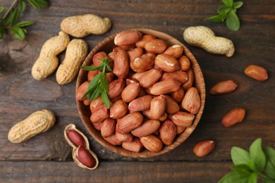 Photo of Fresh peanuts and leaves in bowl on wooden table, flat lay