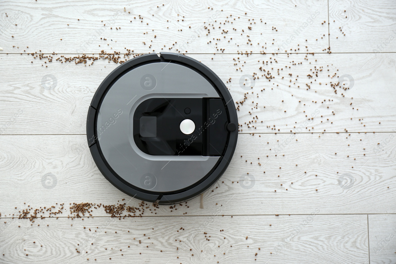 Photo of Modern robotic vacuum cleaner removing scattered buckwheat from wooden floor, top view