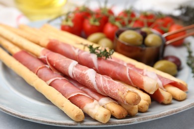 Delicious grissini sticks with prosciutto and snacks on white table, closeup