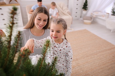 Mother with daughter decorating Christmas tree together at home