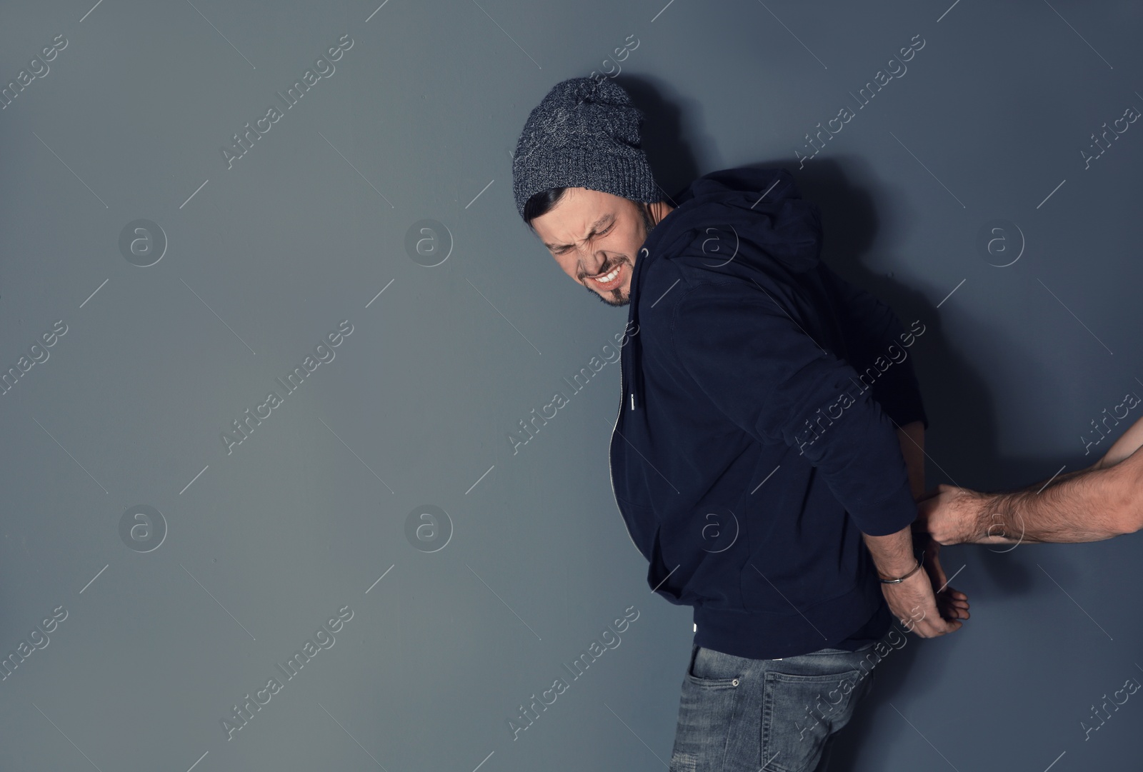 Photo of Man putting handcuffs on drug dealer against grey background. Space for text