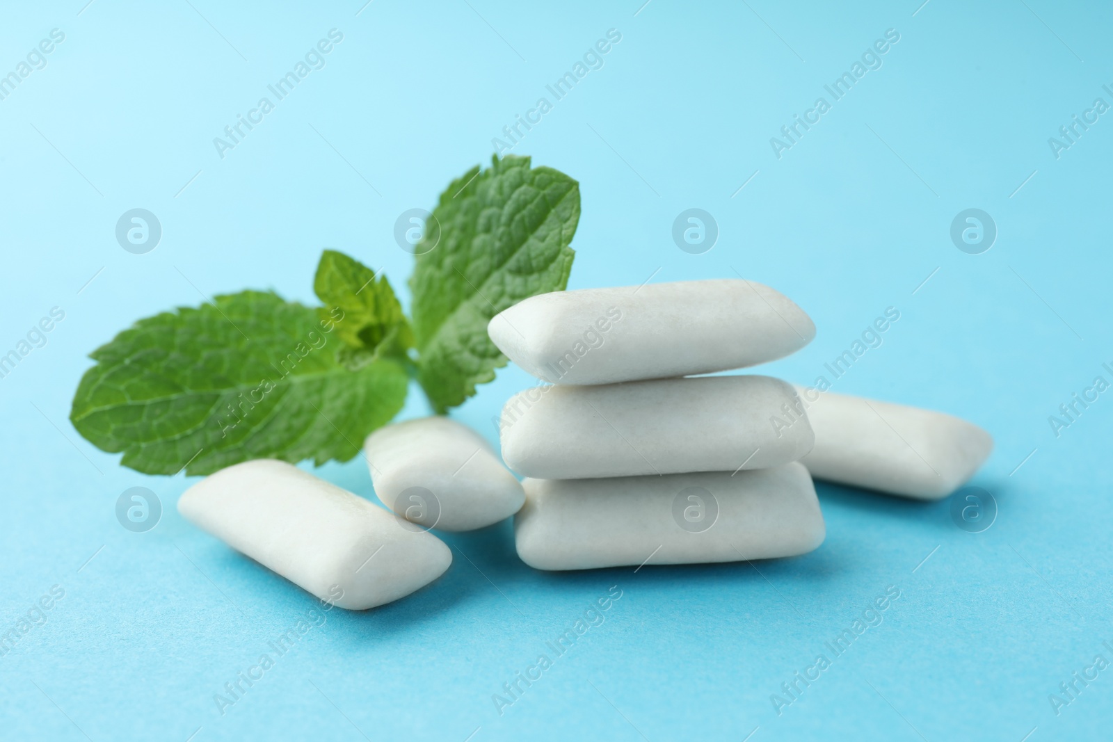 Photo of Tasty white chewing gums and mint leaves on light blue background, closeup