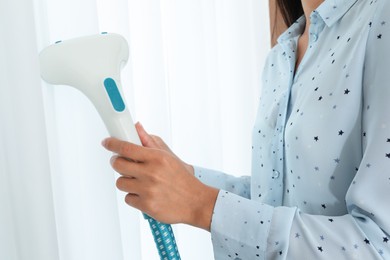 Woman steaming curtain near window at home, closeup