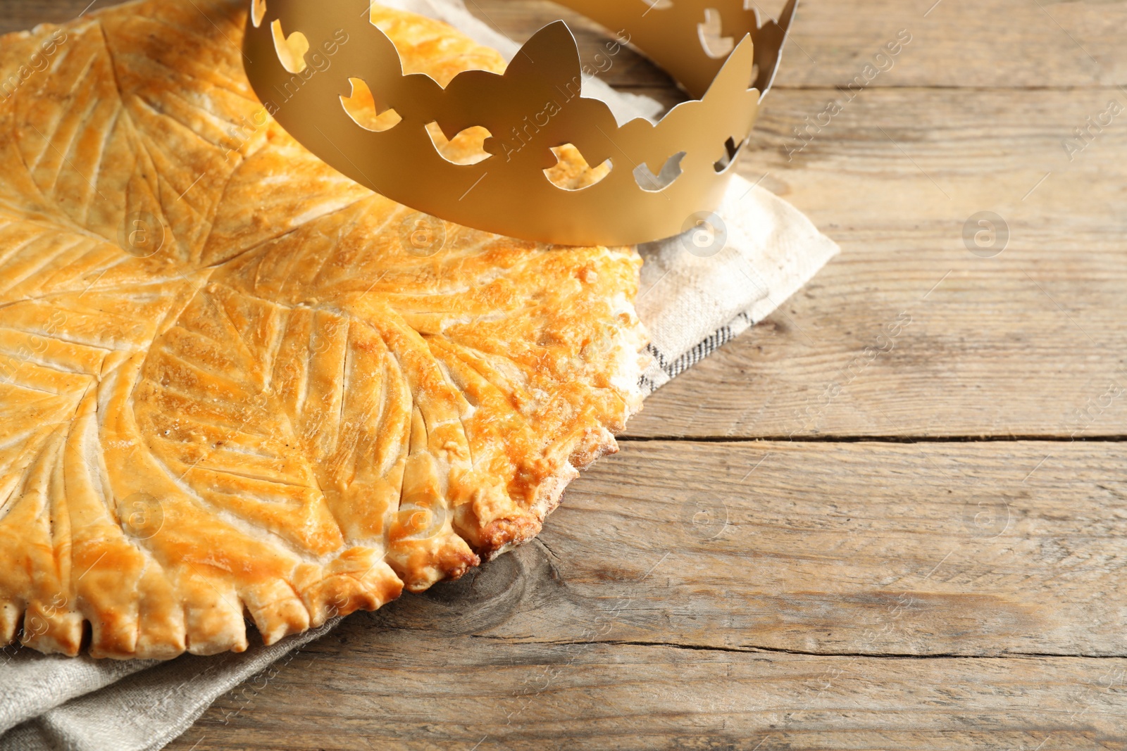 Photo of Traditional galette des Rois with paper crown on wooden table. Space for text