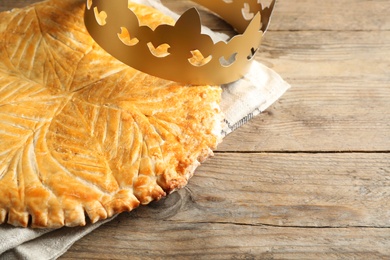 Traditional galette des Rois with paper crown on wooden table. Space for text