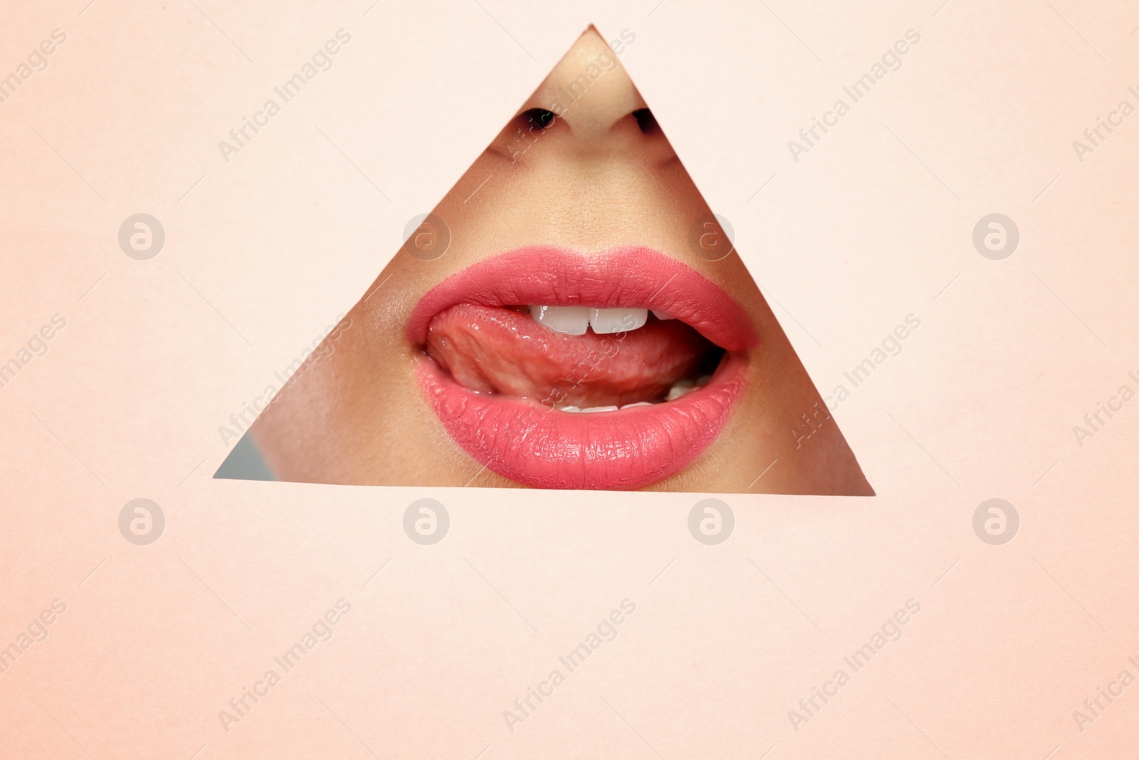 Photo of Young woman wearing beautiful lipstick, view through hole in color paper