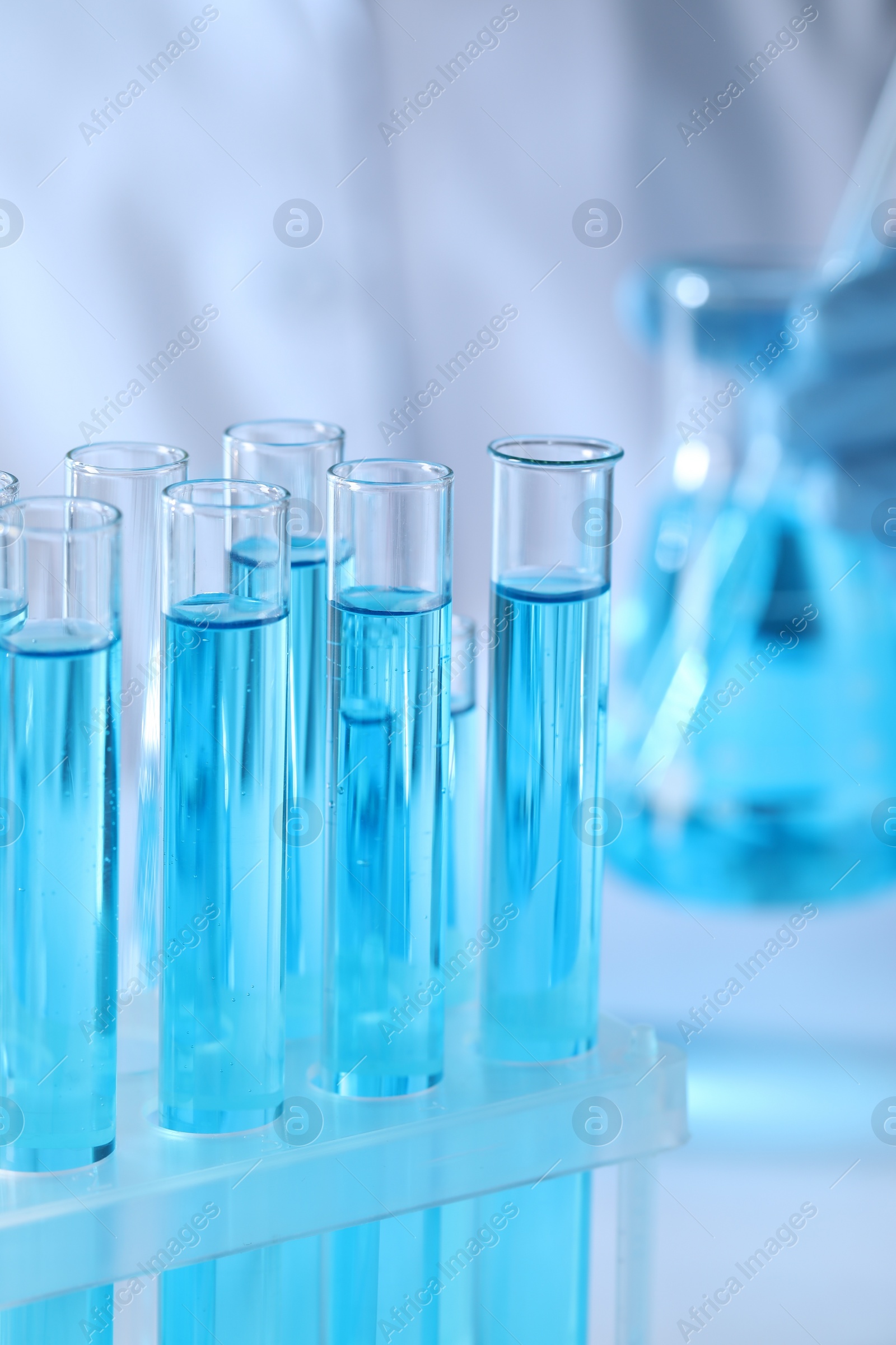 Photo of Scientist holding flask near test tubes with light blue liquid, selective focus