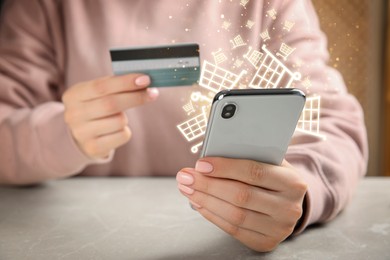 Image of Woman with credit card using smartphone for online purchases at table, closeup. Shopping cart icons flying out of device screen