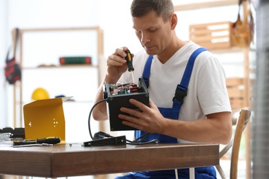 Photo of Professional technician repairing electric fan heater with screwdriver at table indoors