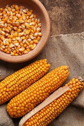 Delicious ripe corn cobs and bowl with seeds on wooden table, flat lay