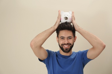 Photo of Portrait of happy young man with piggy bank on color background. Money saving