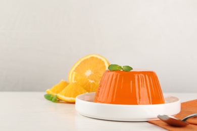 Plate with tasty orange jelly served on white table, space for text