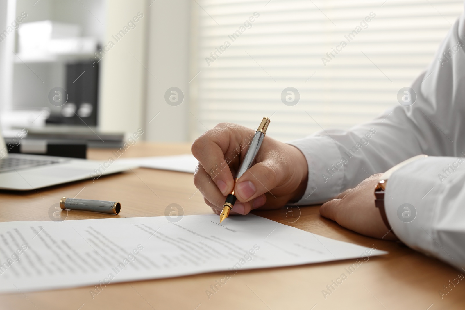 Photo of Notary signing document at wooden table in office, closeup