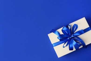 Photo of Beautiful gift box with bow on blue background, top view. Space for text