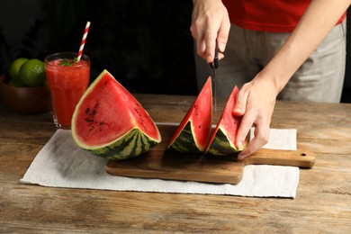 Photo of Woman cutting delicious watermelon at wooden table against dark background, closeup