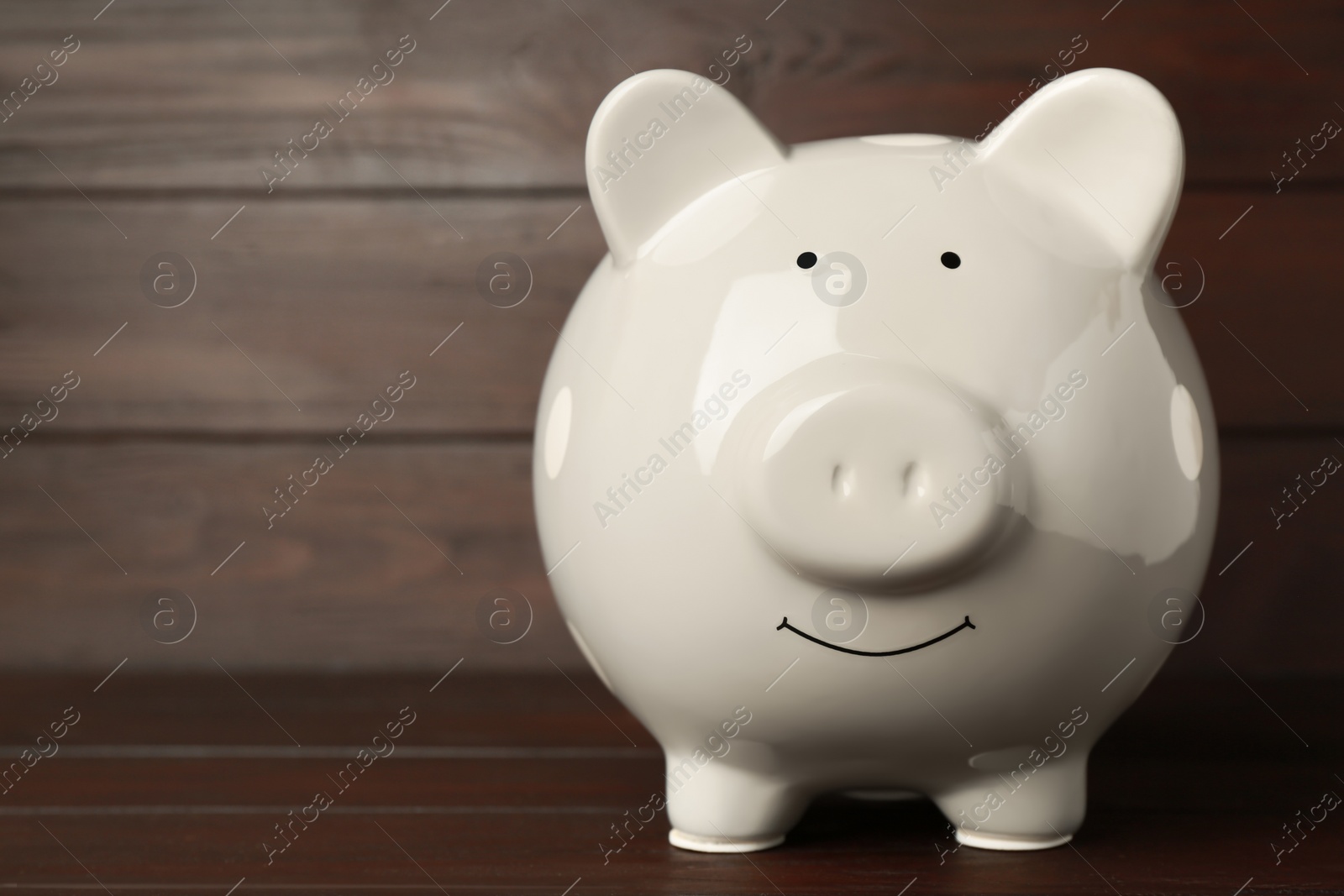 Photo of Ceramic piggy bank on wooden table, closeup. Space for text