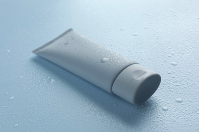 Moisturizing cream in tube on light blue background with water drops, closeup