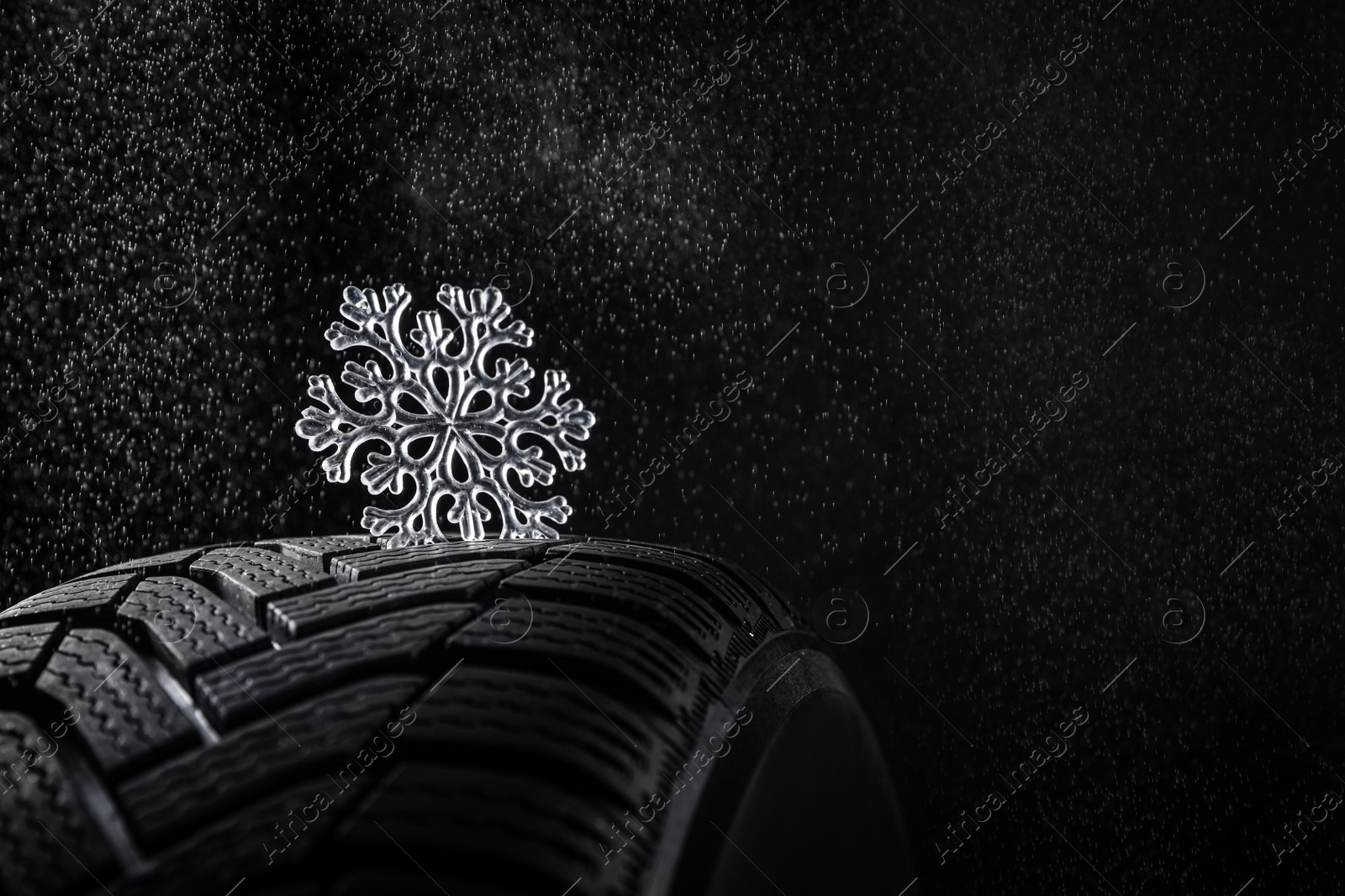 Photo of Winter tire with icy snowflake on black background, closeup. Space for text